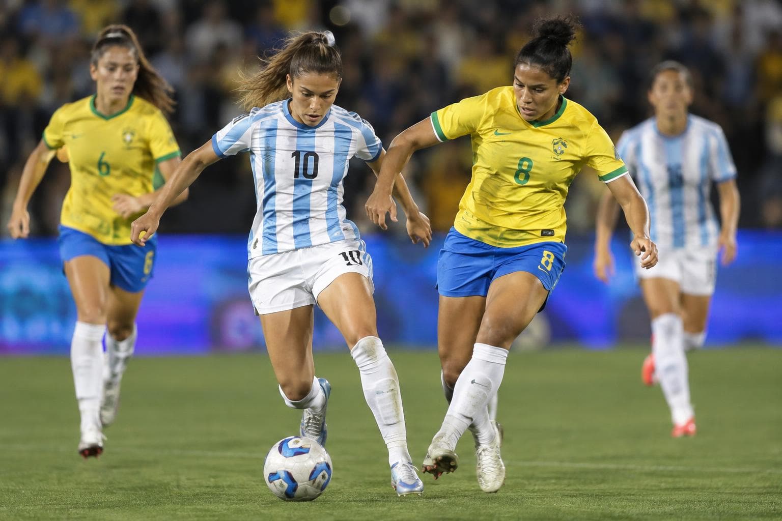Women footballers challenging for the ball in a night stadium.