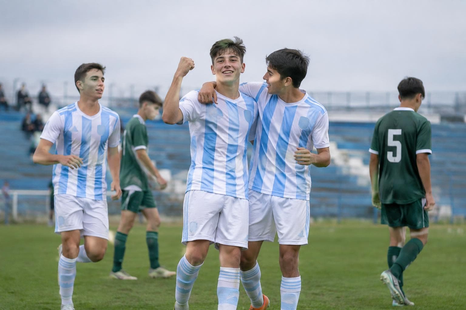 Youth footballers celebrating on a grass pitch, with no visible logos.