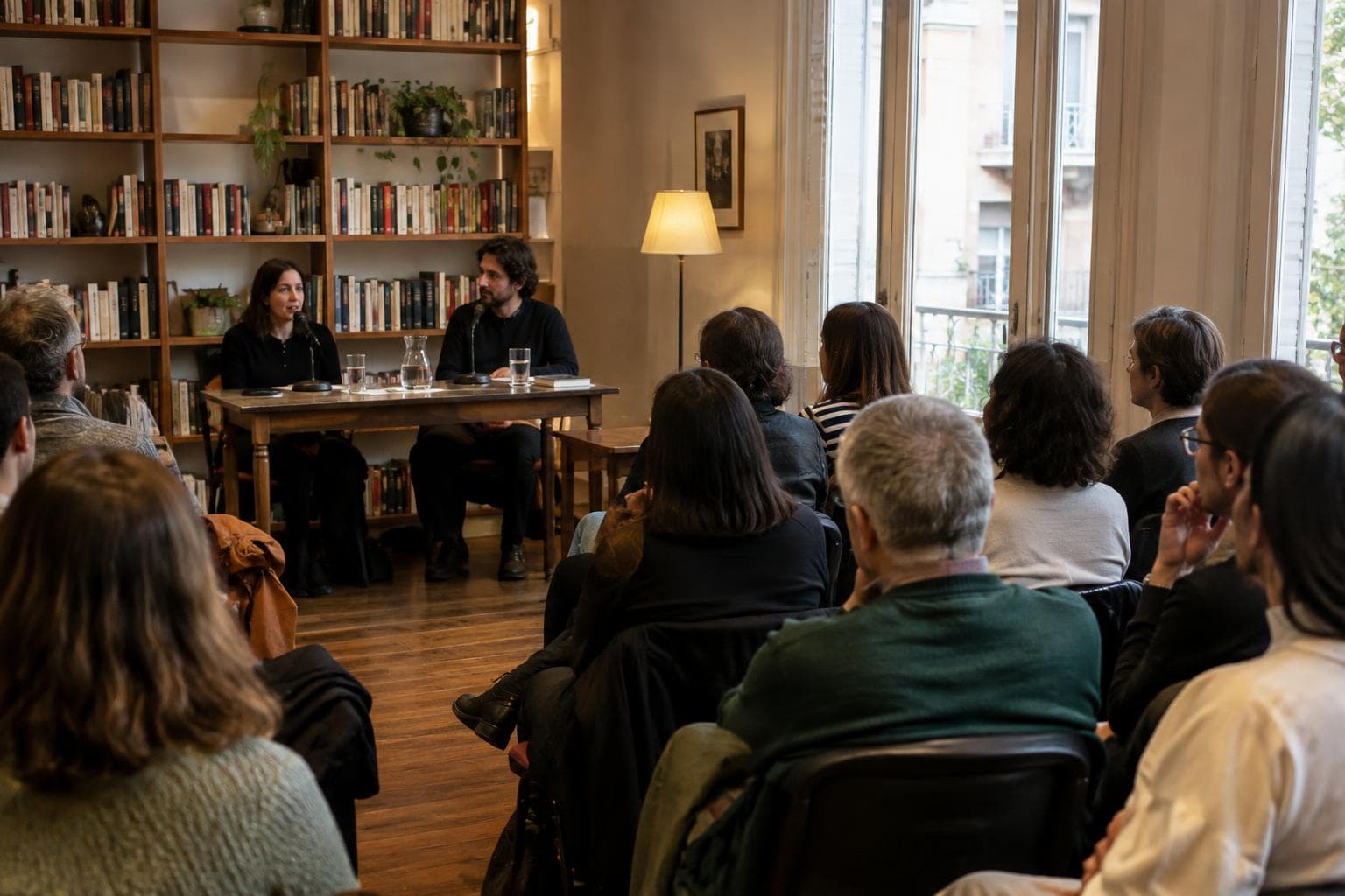 Una charla literaria en una sala cultural, con público sentado y luz cálida; escena ilustrativa, no foto real del festival.