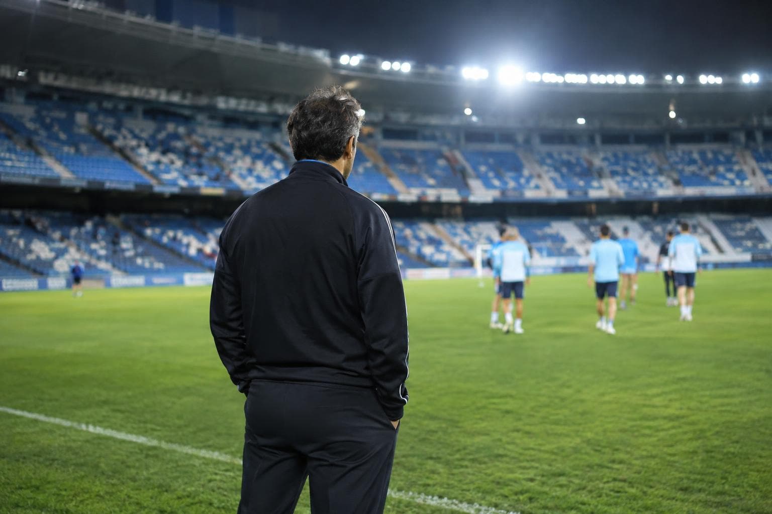 A coach looking across a lit football pitch after a match.