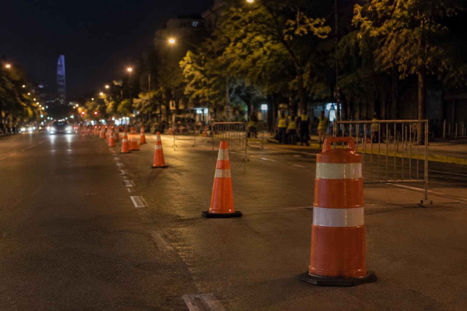 A nighttime road closure with cones and barriers on an urban avenue.