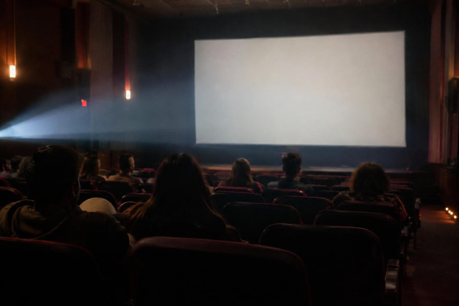 Una sala de cine independiente con público de espaldas y luz de proyector, ilustrativa y no documental.