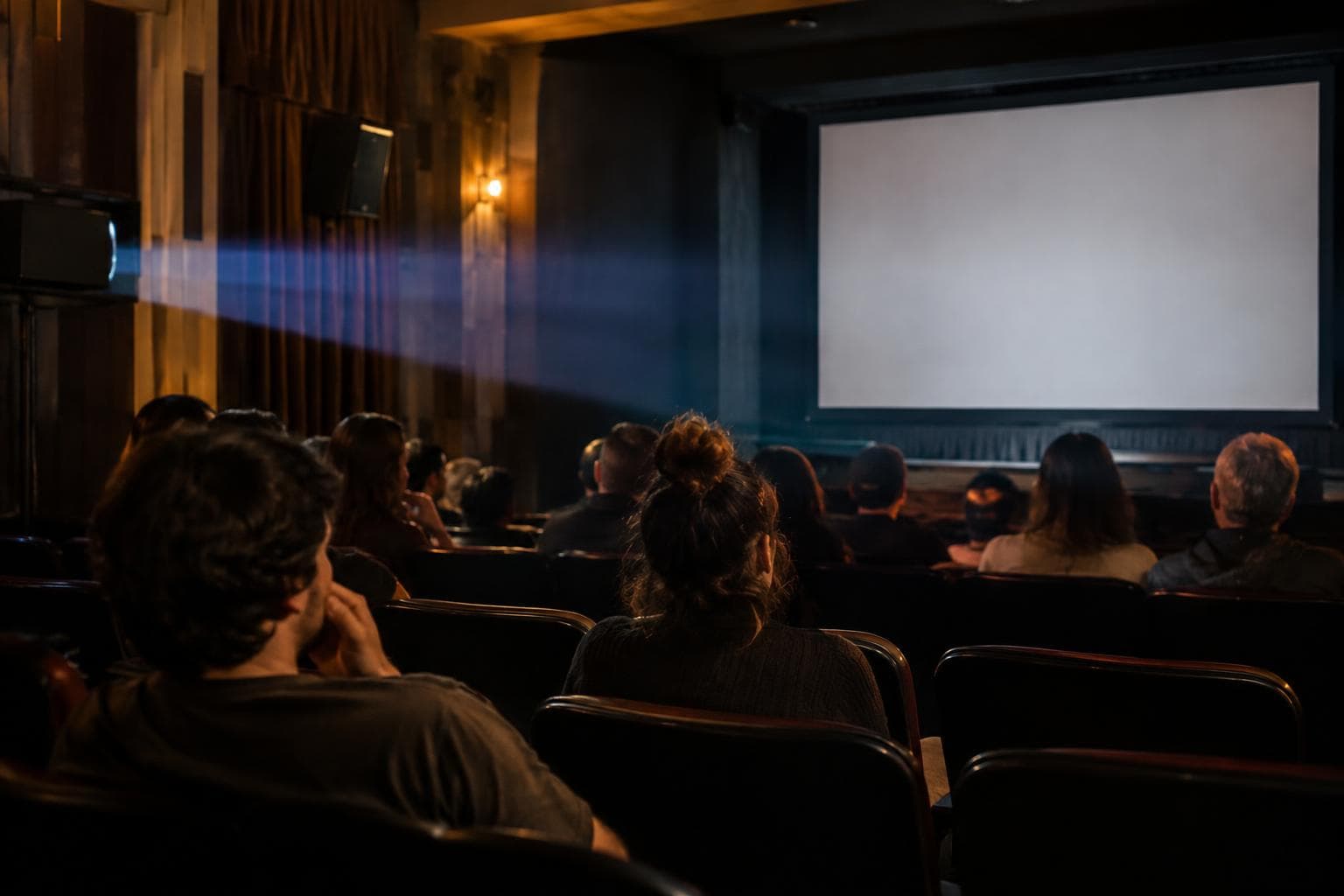 Una sala de cine independiente con público y luz de proyector, ilustrativa y no documental.