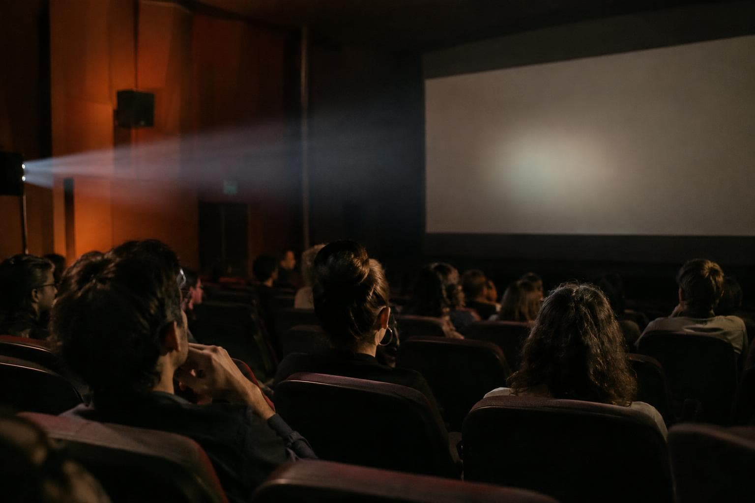 AI-generated photorealistic image of an independent cinema auditorium with an audience and projector light.