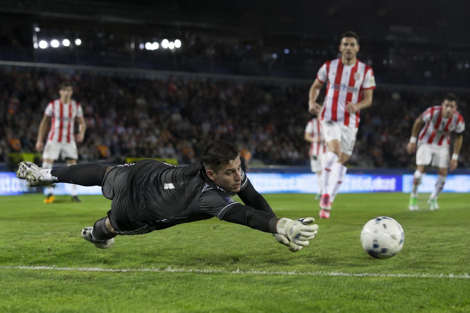 Un arquero atajando un penal en un estadio nocturno.