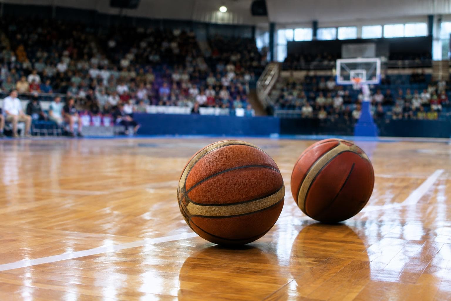 An indoor basketball court with balls in the foreground and blurred stands.