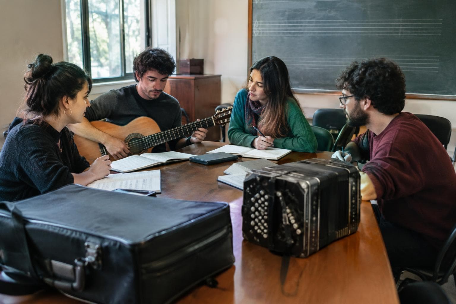 Músicos y estudiantes reunidos en un aula universitaria con guitarra y partituras.