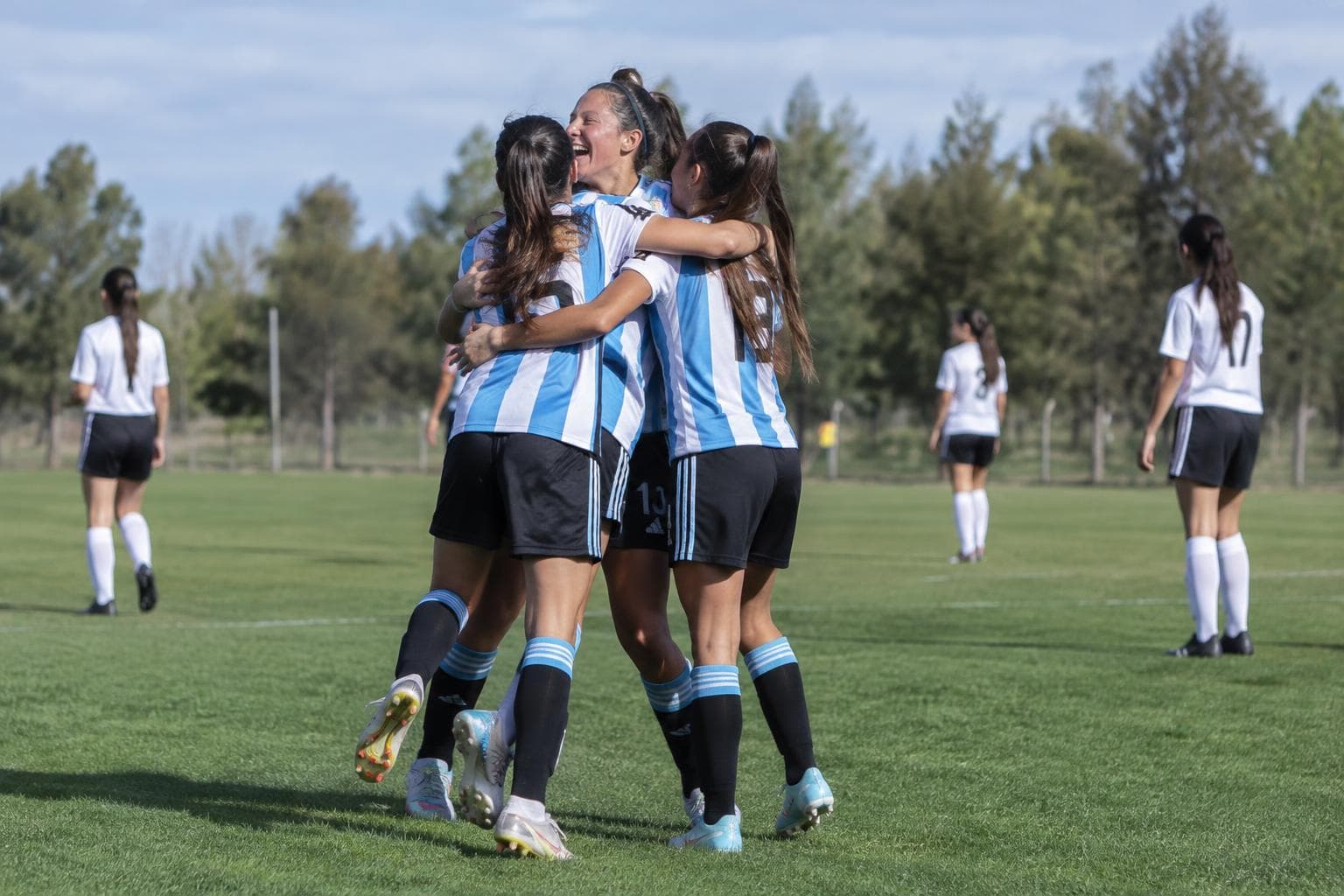 Juveniles argentinas celebrando en una cancha de fútbol.