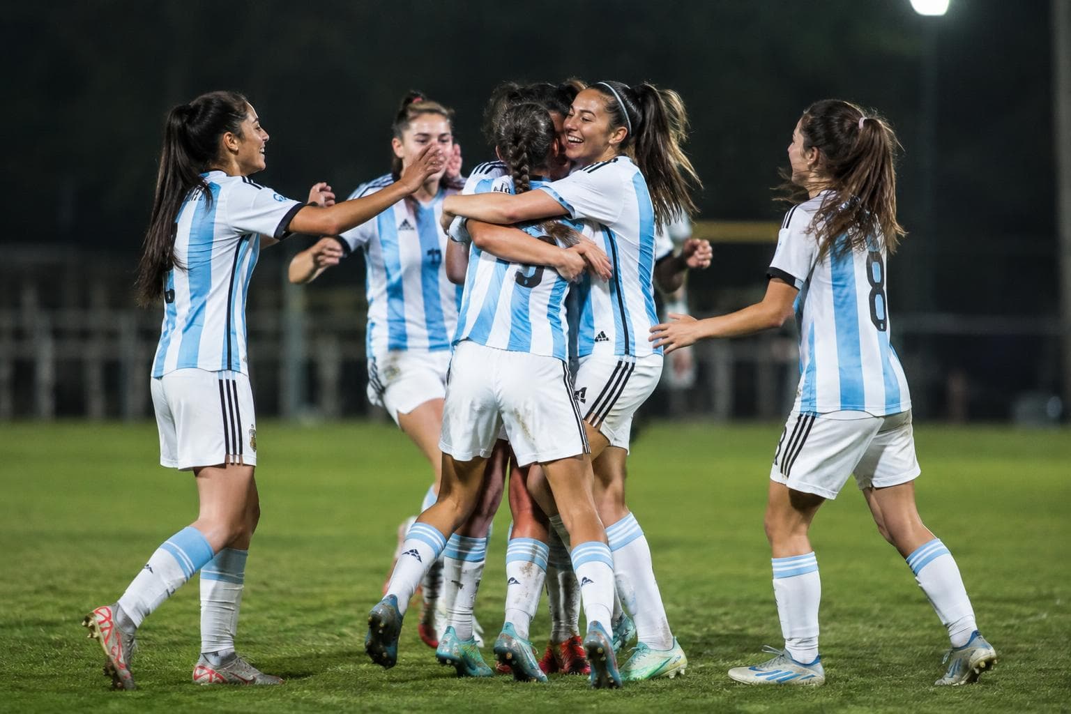 Futbolistas juveniles celebrando en una cancha iluminada.